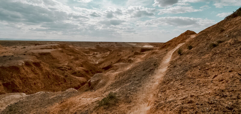 One of the trails at the Flaming Cliffs. Learn about hiking the Flaming Cliffs in Gobi, Mongolia. These cliffs are famous for the dinsoaur eggs and fossils that were discovered there. The Flaming Cliffs now offer a stunning sunset setting as the bright red and orange cliffs look aflame. #mongolia #hiking #flamingcliffs