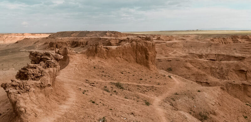 Some of the trails at Flaming Cliffs. Learn about hiking the Flaming Cliffs in Gobi, Mongolia. These cliffs are famous for the dinsoaur eggs and fossils that were discovered there. The Flaming Cliffs now offer a stunning sunset setting as the bright red and orange cliffs look aflame. #mongolia #hiking #flamingcliffs
