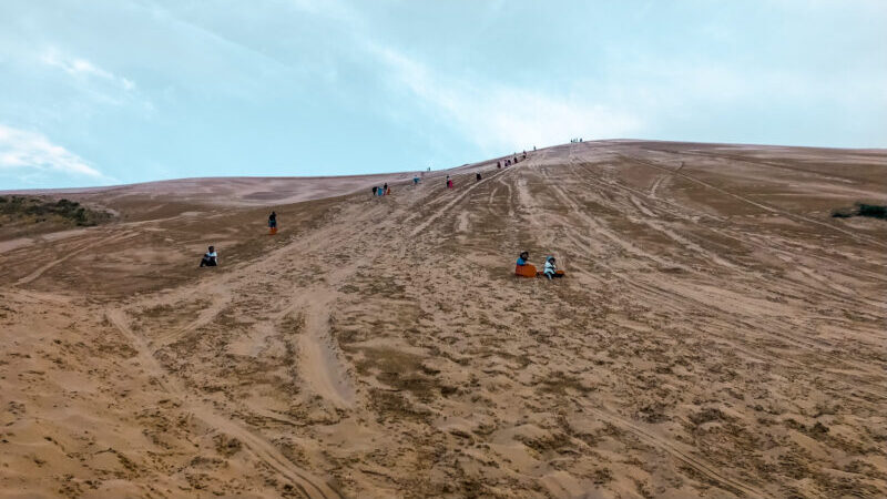 Sledding down the Khongor Sand Dunes. The Gobi in Mongolia is famous for the sand dunes. Therefore climbing the Khongor Sand Dunes is a must-do for any visitor to the Gobi! Learn about what to expect in summiting the great sand dunes. #sanddunes #mongolia #khongorsanddunes
