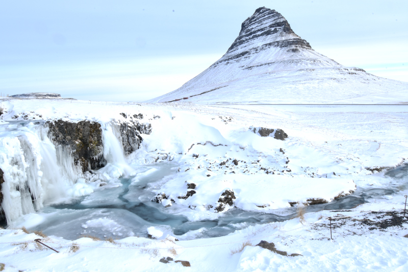 Kirkjufellsfoss Waterfall: Embrace the tranquility of Kirkjufellsfoss in winter, a serene snow-covered landscape framing the captivating view of Kirkjufell Mountain. A picture-perfect scene on a week-long road trip through Iceland in winter.